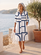 Elegant Spanish woman over 50 walking a sunlit Mediterranean promenade in the white midi shirt dress with a navy geometric line print