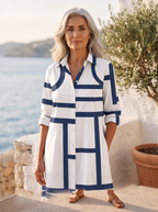 Close detail of the white shirt dress showing the navy geometric line print, classic collar, button placket and rolled sleeve