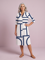 Spanish woman over 50 in the white shirt dress with a navy geometric line print, studio three-quarter pose on a soft lilac backdrop