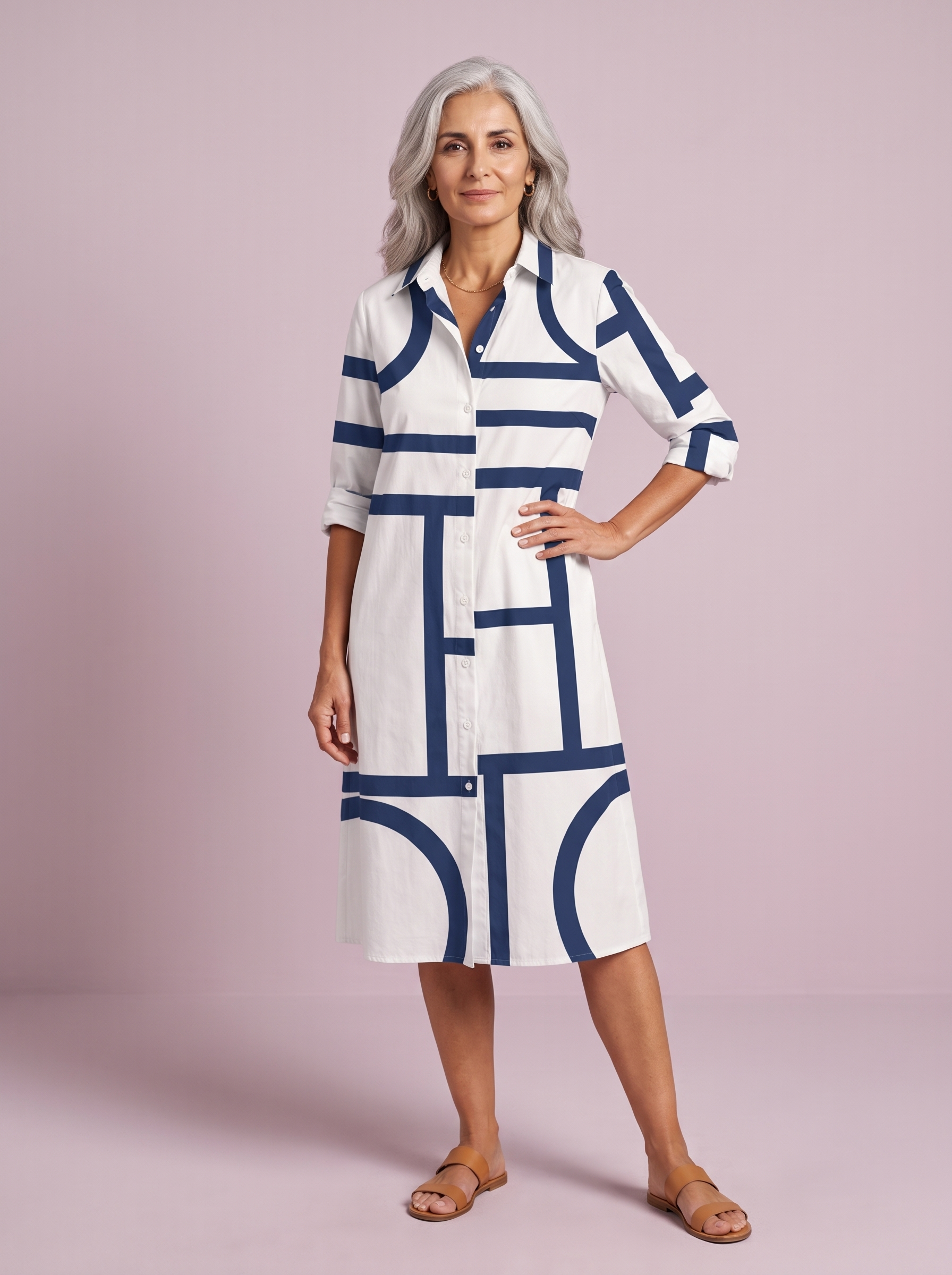 Spanish woman over 50 in the white shirt dress with a navy geometric line print, studio three-quarter pose on a soft lilac backdrop