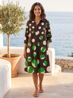 Spanish woman over 50 with chestnut hair on a Mediterranean coastal terrace in the chocolate-brown polka-dot shirt dress