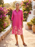 Spanish woman in her fifties with silver hair in a bun, in a Mediterranean garden with bougainvillea, wearing the fuchsia botanical shirt dress
