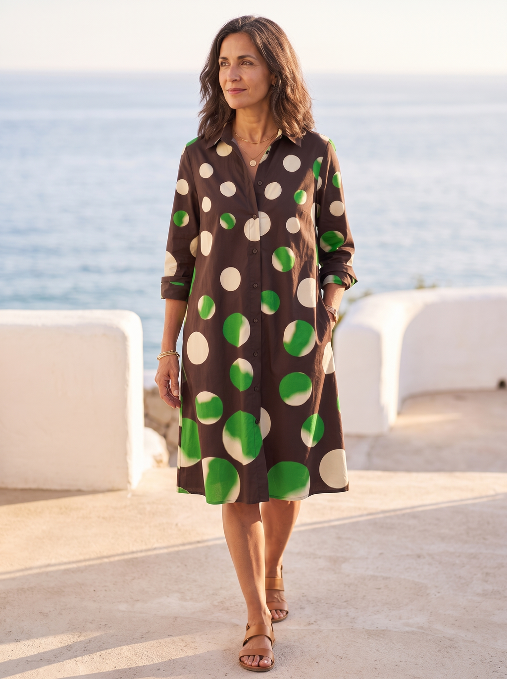 Spanish woman over 50 walking a sunlit coastal promenade in the chocolate-brown polka-dot shirt dress