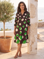 Spanish woman over 50 leaning by a whitewashed wall with an olive tree in the polka-dot shirt dress