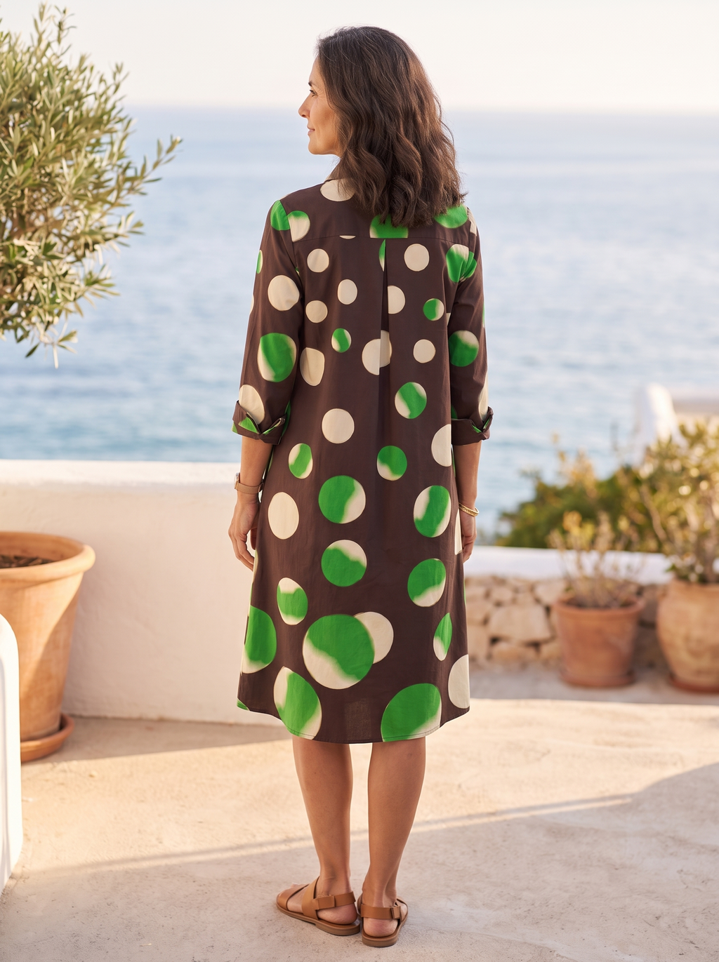 Back view of the chocolate-brown polka-dot shirt dress on a Mediterranean coastal terrace