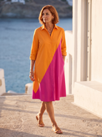 Spanish woman over 50 walking a sunlit coastal promenade in the orange and magenta colour-block shirt dress